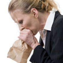 woman breathing into a brown paper bag how to help someone with a panic attack